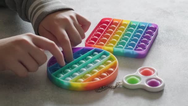 Onherkenbaar kind duwt bellen op kleurrijke poppit speelgoed met vingers aan tafel — Stockvideo