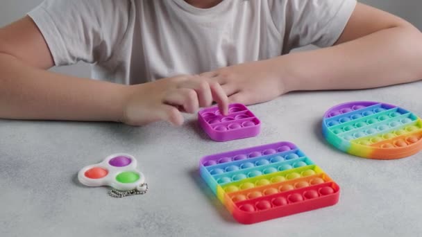 Enfant méconnaissable pousse des bulles sur le jouet poppit coloré avec les doigts à la table — Video