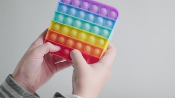 Kind spielt, schiebt Blasen auf angesagtem Regenbogenmohn-Fidget-Spielzeug mit den Fingern — Stockvideo