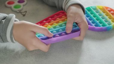 Tanınmayan çocuk masasında parmakları olan renkli poppit oyuncağına baloncuklar fırlatıyor.