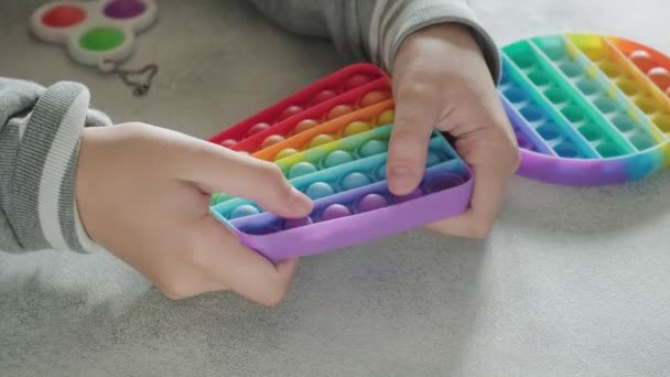 Неузнаваемый ребенок толкает пузыри на красочную игрушку с пальцами за столом — стоковое видео