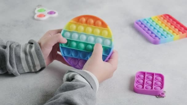 Unerkennbares Kind schiebt mit Fingern am Tisch Blasen auf buntes Mohnspielzeug — Stockvideo
