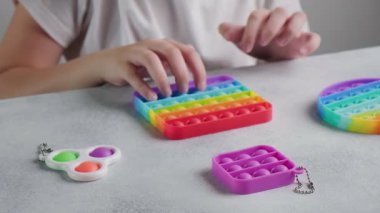 Tanınmayan çocuk masasında parmakları olan renkli poppit oyuncağına baloncuklar fırlatıyor.