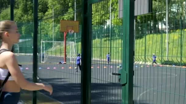 Junges, athletisches blondes Mädchen mit Pferdeschwanz in Sportbekleidung betritt Sportplatz — Stockvideo