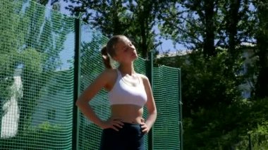Spor giyimli sarışın seksi kadın spor sahasında boynunu esnetiyor.