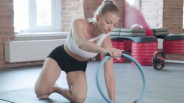 Genç, beyaz, formda, sportif bir kadın spor salonunda pilates halkasıyla kalas egzersizi yapıyor.