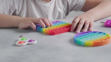 Tanınmayan çocuk masasında parmakları olan renkli poppit oyuncağına baloncuklar fırlatıyor.
