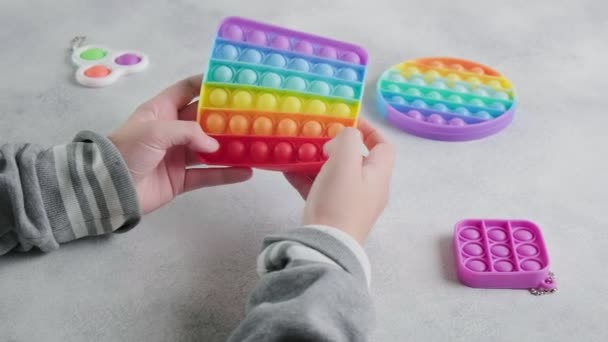 Unrecognizable child pushes bubbles on colorful poppit toy with fingers at table — Stock Video