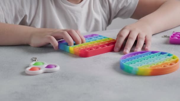 Niño irreconocible empuja burbujas en colorido juguete poppit con los dedos en la mesa — Vídeo de stock