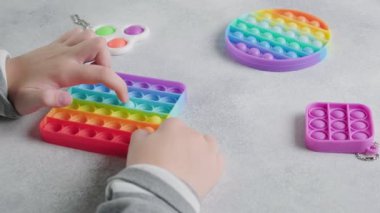 Tanınmayan çocuk masasında parmakları olan renkli poppit oyuncağına baloncuklar fırlatıyor.