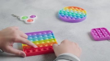 Tanınmayan çocuk masasında parmakları olan renkli poppit oyuncağına baloncuklar fırlatıyor.