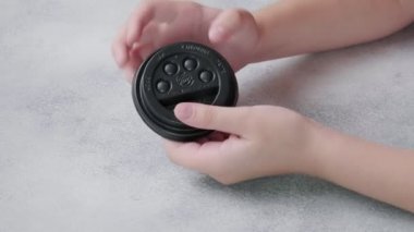 Çocuk, parmaklarıyla kahve fincanının siyah plastik kapağına poppit baloncukları itiyor.