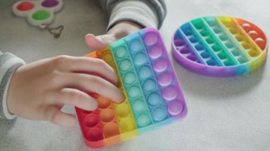 Tanınmayan çocuk masasında parmakları olan renkli poppit oyuncağına baloncuklar fırlatıyor.