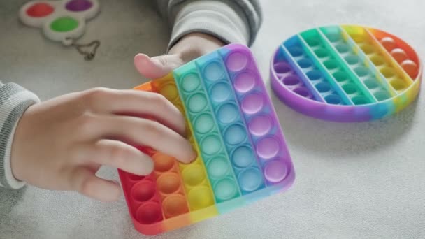 Enfant méconnaissable pousse des bulles sur le jouet poppit coloré avec les doigts à la table — Video