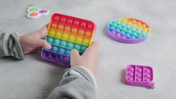 Нерозпізнана дитина штовхає бульбашки на барвисту іграшку поппіт з пальцями за столом — стокове відео