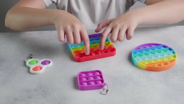 Felismerhetetlen gyermek nyomja buborékok színes poppit játék ujjak az asztalnál — Stock videók