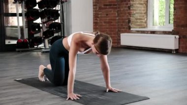 Genç, zayıf, beyaz bir kadın köpeğe doğru eğilip asana pozu veriyor.