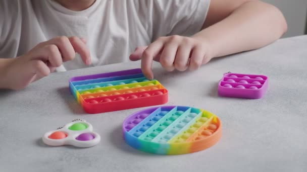 Unrecognizable child pushes bubbles on colorful poppit toy with fingers at table — Stock Video