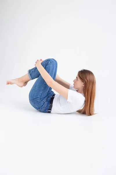 Ung kaukasiska söt flicka i t-shirt och jeans lyfta hennes ben, hålla knän — Stockfoto