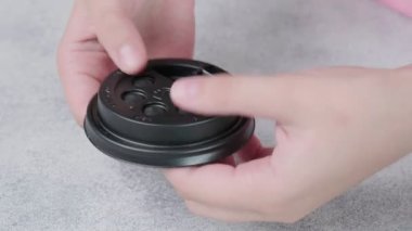 Çocuk, parmaklarıyla kahve fincanının siyah plastik kapağına poppit baloncukları itiyor.