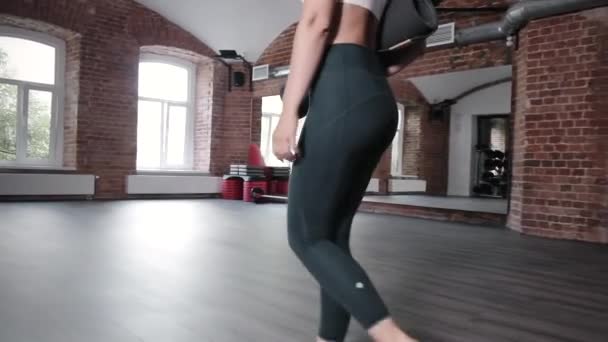Mladá žena ve sportovním oblečení chůze v tělocvičně s podložkou v ruce, připraven na cvičení — Stock video