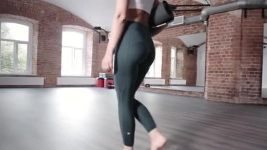 Spor kıyafetli genç bir kadın spor salonunda elinde paspasla yürüyor. Egzersiz yapmaya hazır.