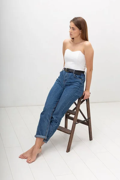 Jovem mulher caucasiana com cabelo castanho longo em espartilho, jeans azul no estúdio — Fotografia de Stock