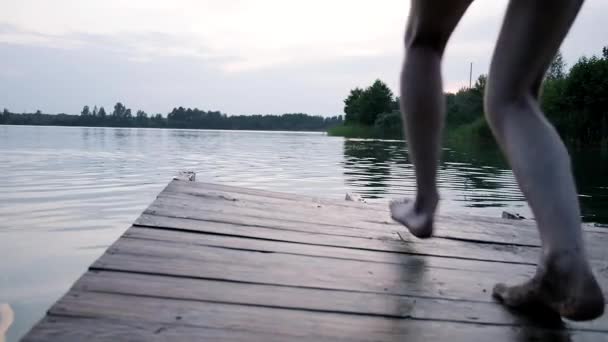 Genç erkek ahşap iskelede koşuyor, top mermisi gibi sıçramalarla göle atlıyor. — Stok video