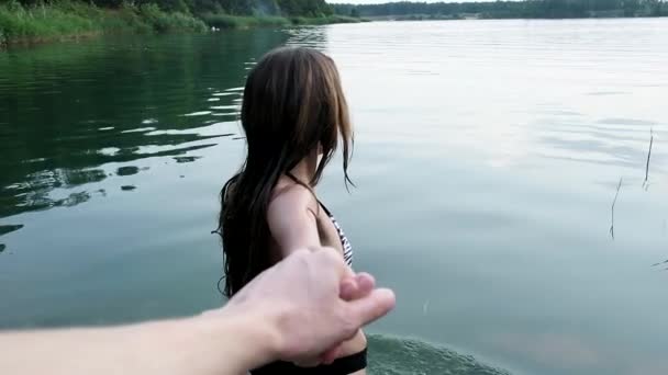 Seductive young fit girl in bikini slowly enters lake to swim holding mans hand — Vídeos de Stock