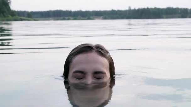 Cabeza de mujer joven que se sumerge en el lago, luego aparece del agua y se ríe — Vídeos de Stock