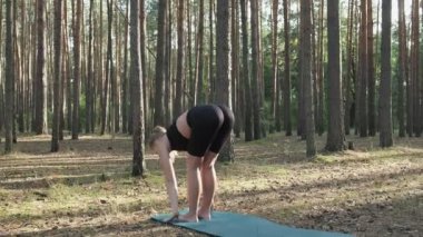 Esnek fit kız yoga yapıyor, güneşli çam ormanlarında surya namaskar yapıyor.