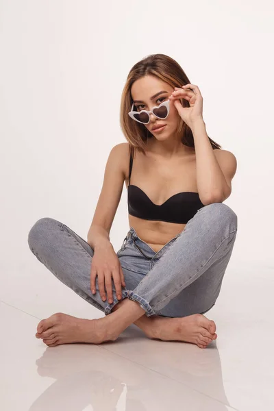 Sexig asiatisk flicka poserar i underkläder, jeans, solglasögon på vit studio bakgrund — Stockfoto