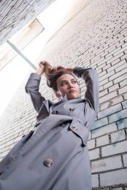 Trençkotlu çekici Asyalı model, alt noktadan duvarın yanında duruyor.