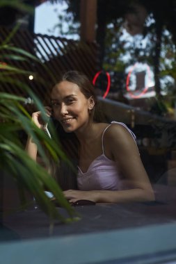 Gülümseyen güzel bayan telefonla arıyor. Kafenin dışındaki cam kırıklarından vurulmuş.