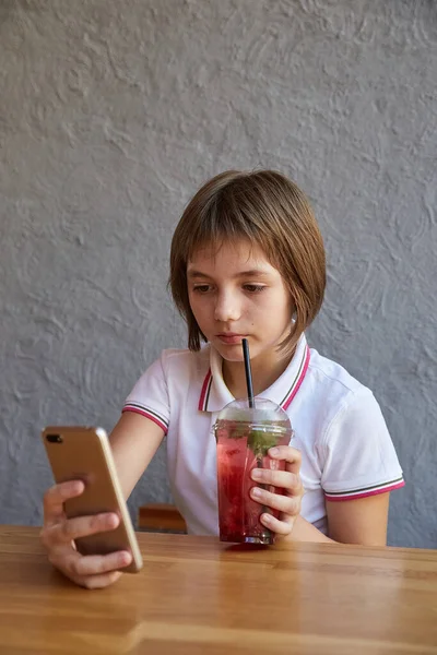 電話で情報を読んだりカフェのテーブルで赤い氷のカクテルを飲んだり — ストック写真