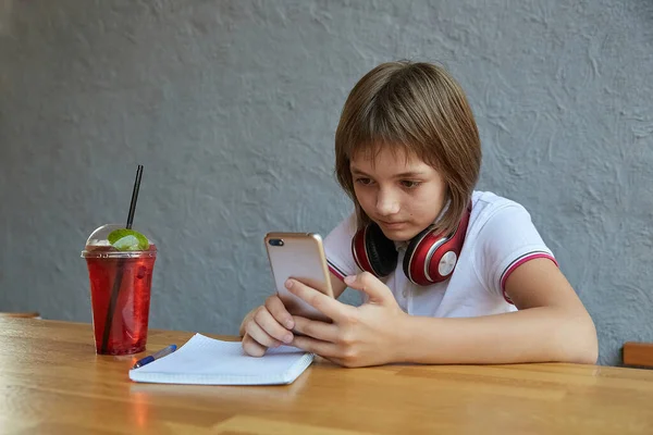 ヘッドフォンと赤い氷のレモネードを持つ女子高生は、スマートフォン、サーフインターネットを使用しています — ストック写真
