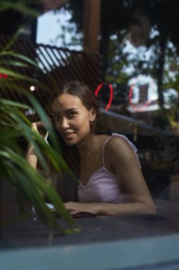 Gülümseyen güzel bayan telefonla arıyor. Kafenin dışındaki cam kırıklarından vurulmuş.