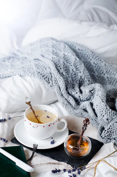 Bandeja con miel y una taza de té caliente en la cama —  Fotos de Stock