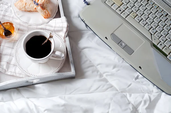 A cup of coffee with the laptop on the bed