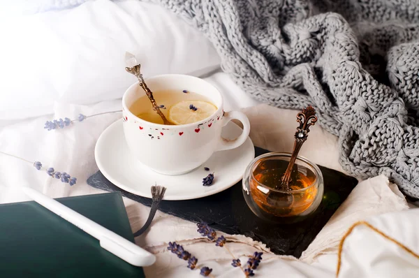 Поднос с медом и чашкой горячего чая в постели — стоковое фото
