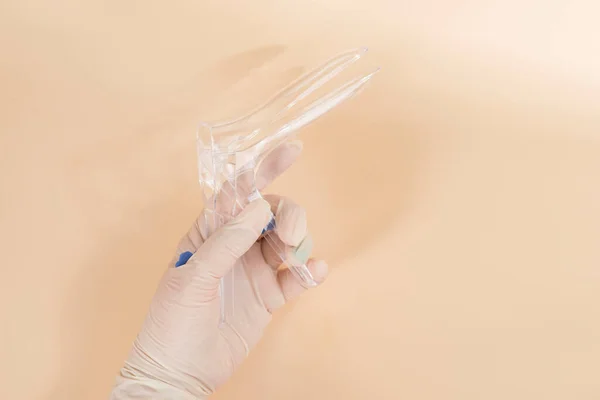 Kvinna läkare som håller vaginal spekulum på beige bakgrund, Medicinska objekt — Stockfoto