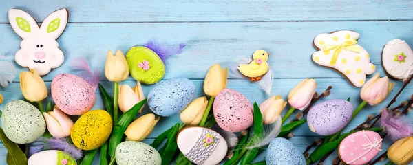 庆祝复活节的糖果框架 姜饼的形状是复活节兔子 彩蛋和郁金香 蓝色背景顶部视图复制空间 — 图库照片