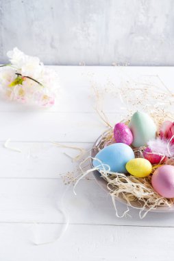 Beyaz ahşap kaplamalı küçük bir yuvada renkli paskalya yumurtaları, kopyalama alanı. Tatil etkinliği düzleştirildi