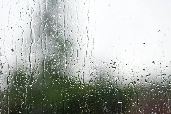 Arkaplanda yeşil ağaç olan pencereye yağmur damlaları yağar