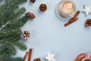 Kahve fincanı, çam kozalağı, tarçın çubukları ve açık mavi arkaplanda köknar dalları ile kış düzlüğü.