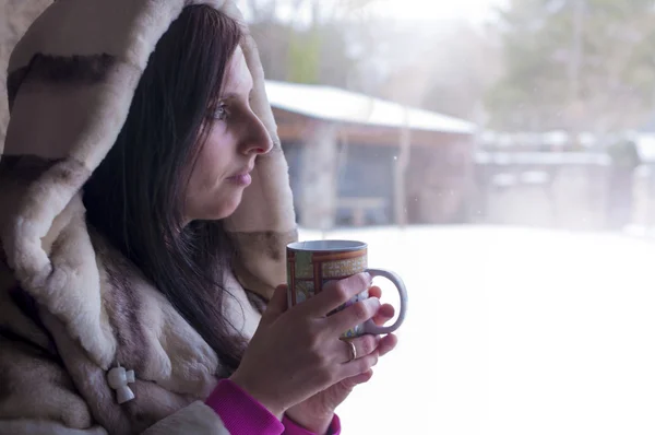 Woman drinking tea in the window watching the cold winter day meaning through the window