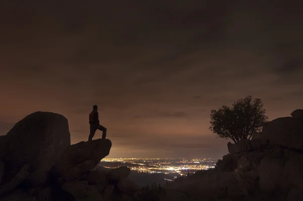 Homem olha para as luzes da cidade do topo da montanha — Fotografia de Stock