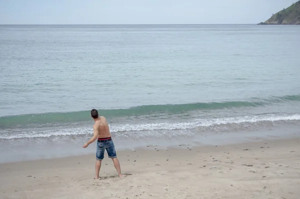 L'uomo gioca lanciando sassi sulla spiaggia — Foto Stock