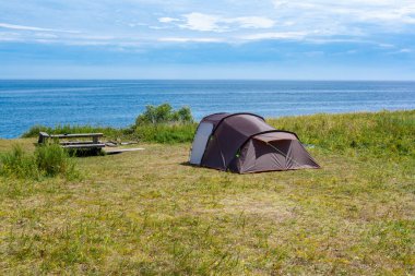 Baykal Gölü 'nün yanındaki çimlerin üzerinde sıraları ve masaları olan yürüyüş yerinde açık bir çadır. Bulutlu mavi gökyüzü ve yaz güneşi.