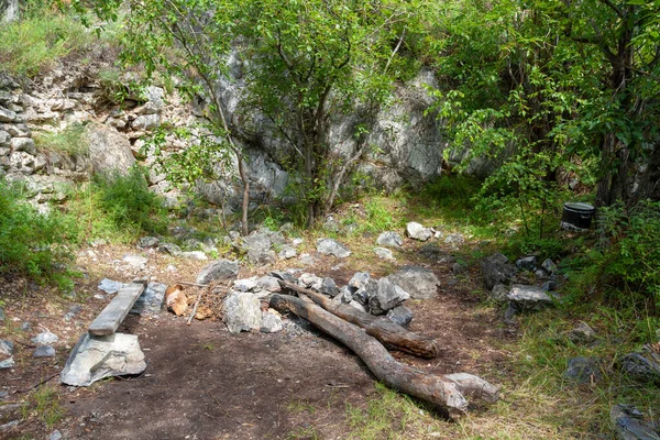 篝火的地方下岩石与长椅和树干 保龄球帽挂在树枝上 周围的大石头和绿色植被 — 图库照片